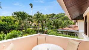 A balcony with a table and chairs, overlooking a lush garden with palm trees and a view of a building with a tiled roof. - Hotel Villa del Sueño (Sardinal)