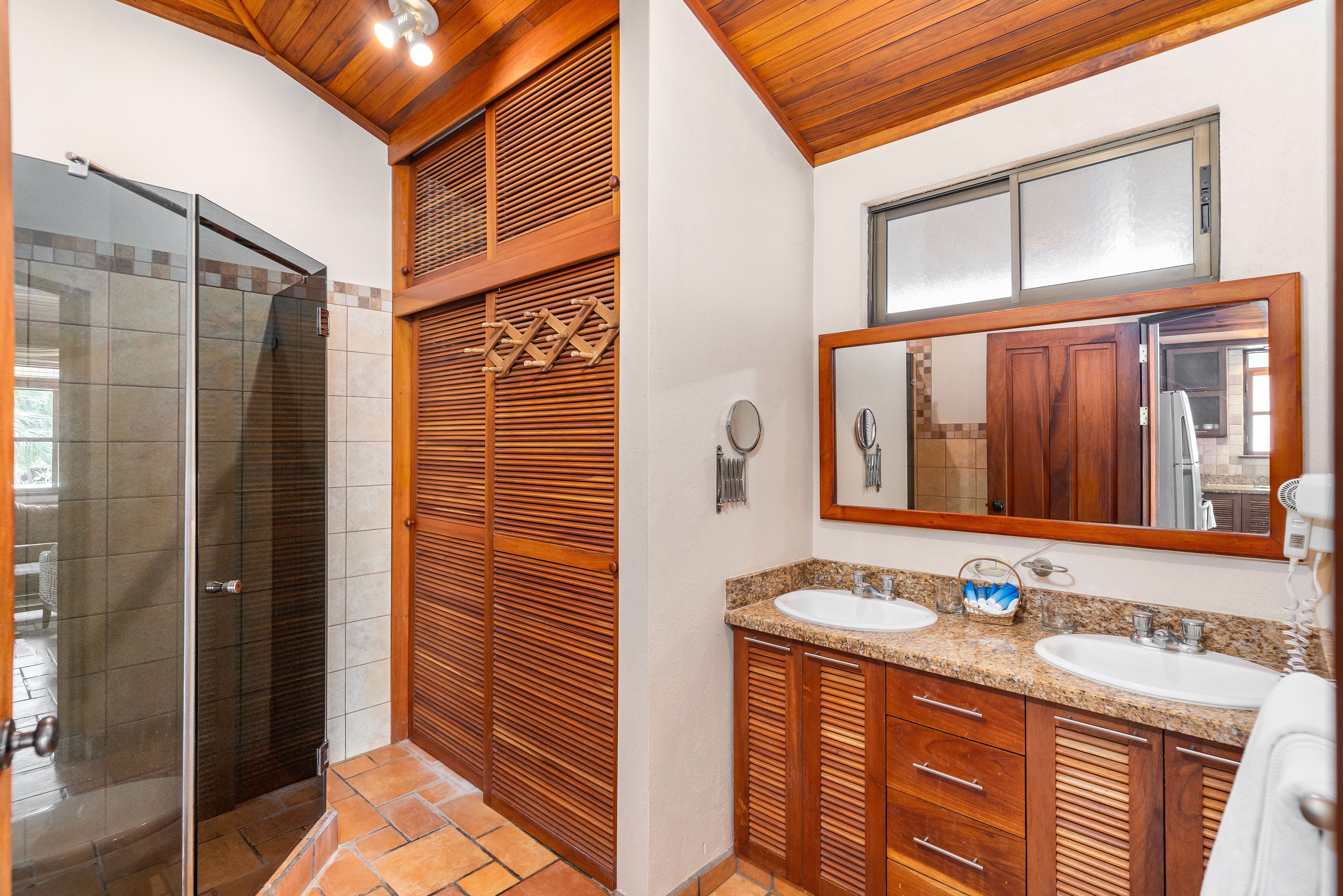 A bathroom with a glass shower enclosure, wooden cabinets, a double sink vanity, and a large mirror.