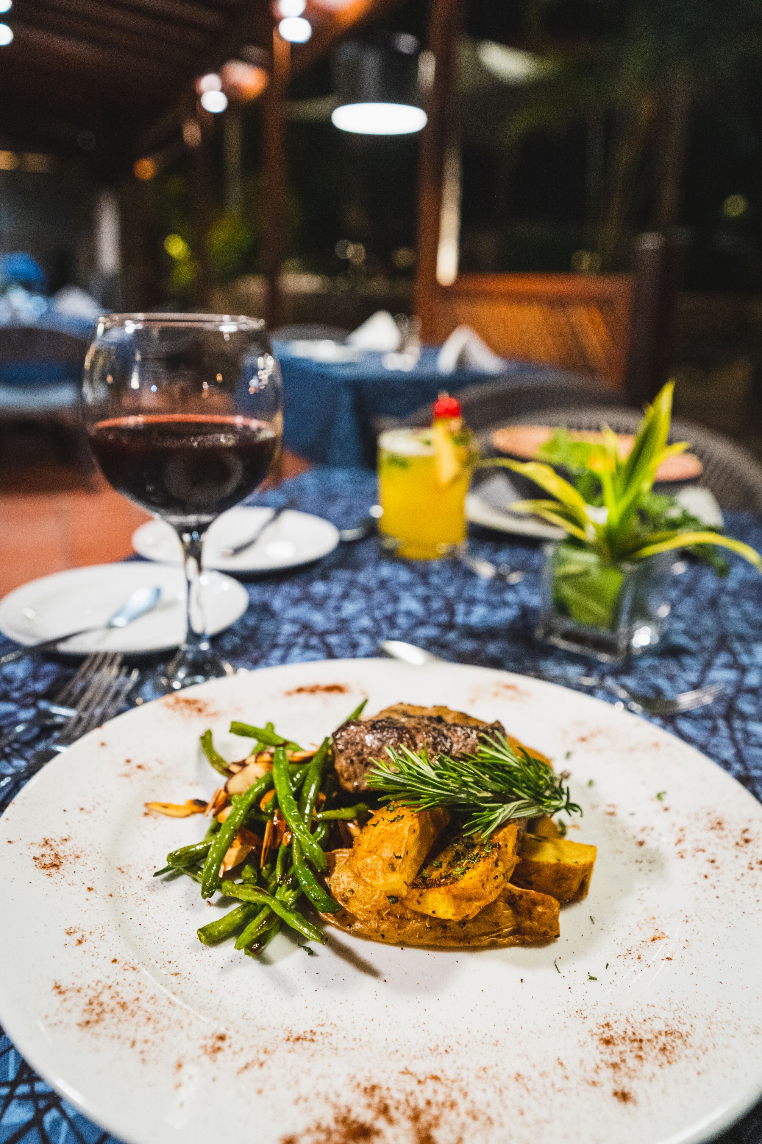 A dining table with a plate of food, a glass of red wine, and a cocktail.