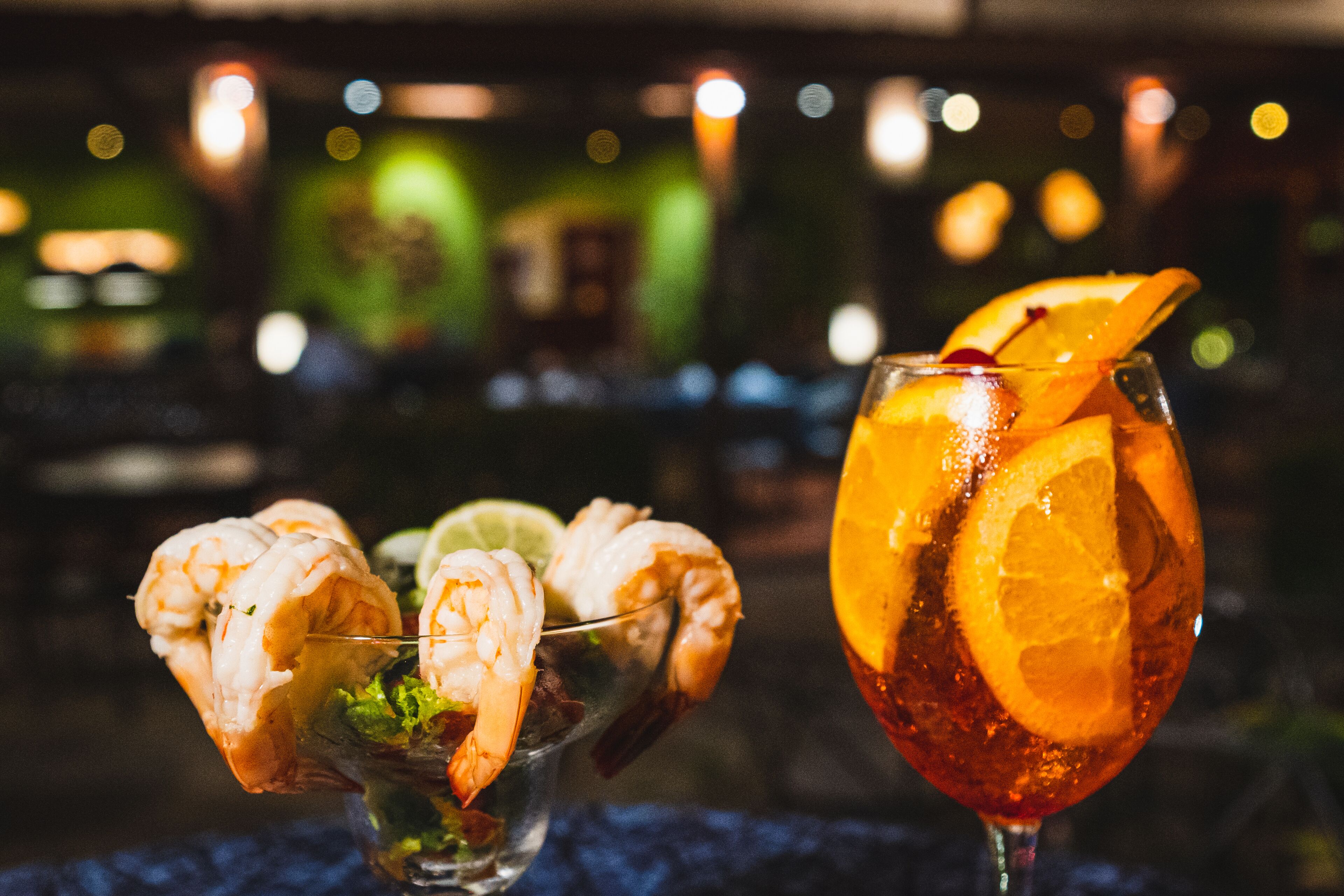 A cocktail with shrimp and citrus garnish, and a glass of iced tea with orange slices.