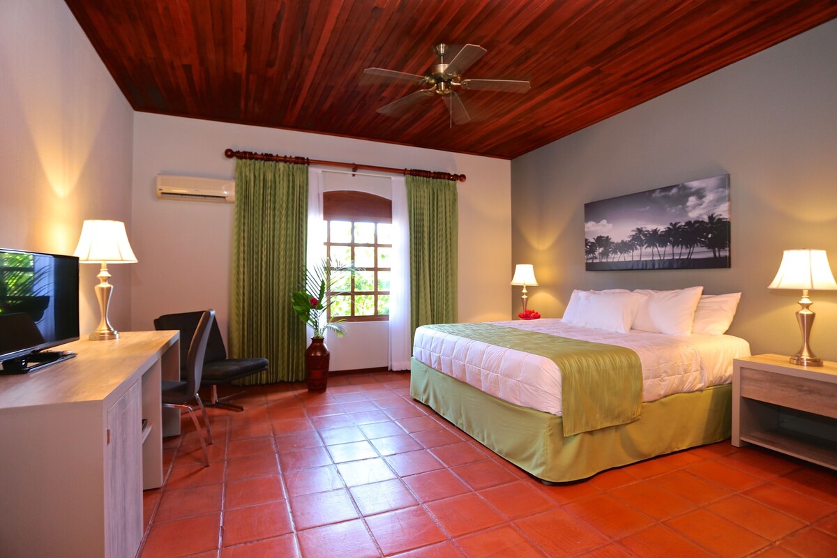 A hotel room with a bed, desk, chair, TV, and a ceiling fan.