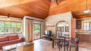 A spacious living area with a wooden ceiling, a stone wall, a TV, and a dining set. - Hotel Villa del Sueño (Sardinal)