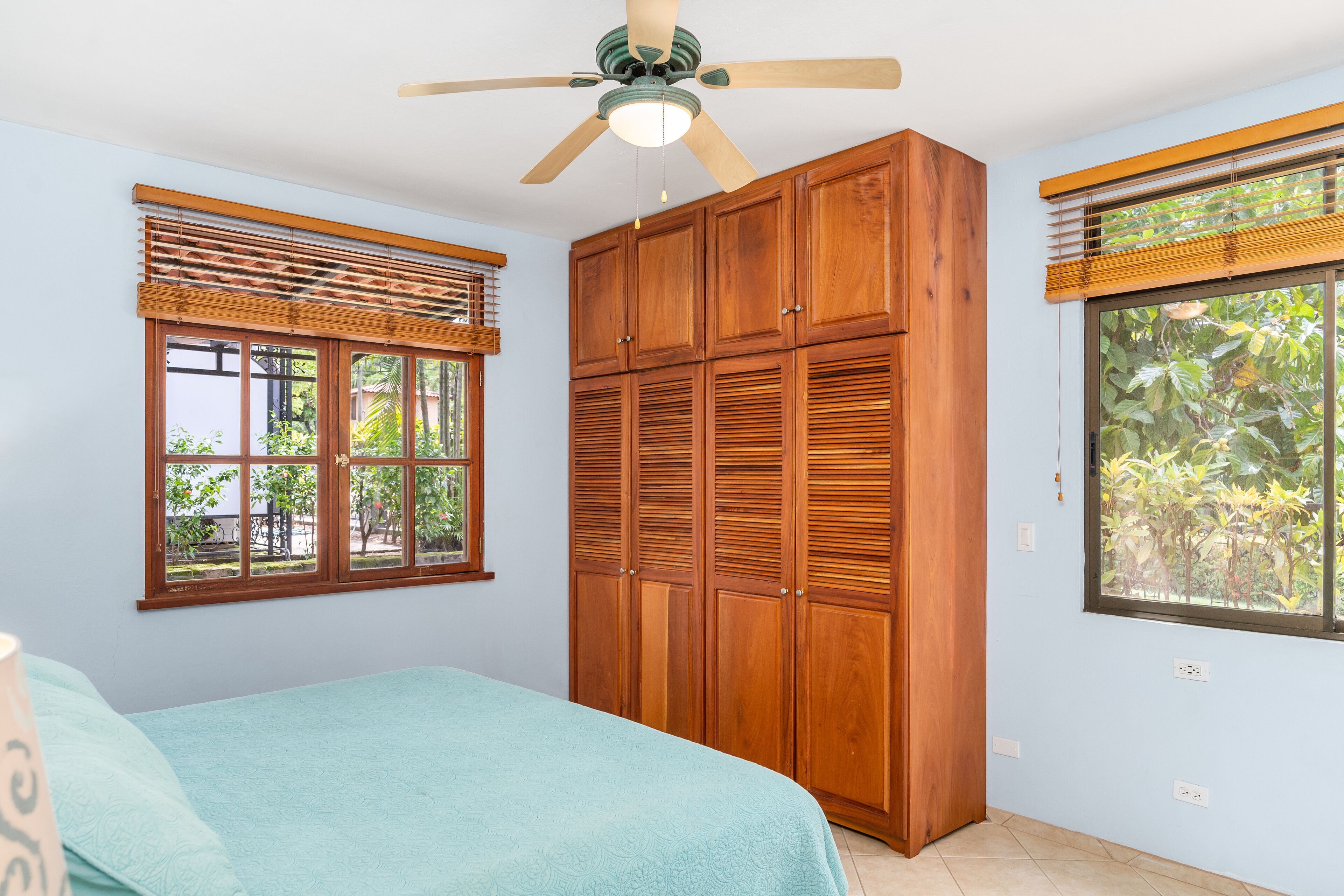 A bedroom with a bed, wooden wardrobe, and a ceiling fan.