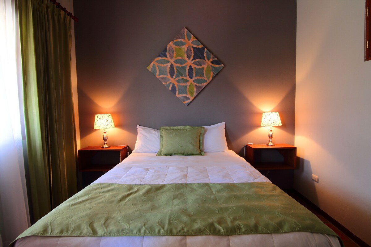 A neatly made bed with a green blanket, two bedside lamps, and a decorative wall piece.