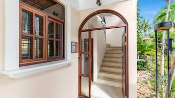 L’entrée d’un immeuble avec une porte en bois, un escalier et une vue sur un jardin agrémenté de rochers et de plantes.
