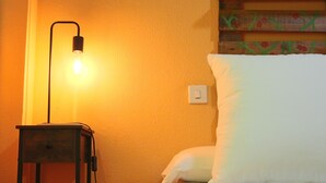 A bed with white pillows and a wooden headboard, a bedside table with a lamp, and a wall with a light switch.