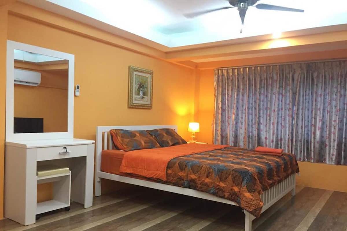 A bedroom with a bed, a dresser, a mirror, a lamp, and a window with curtains.