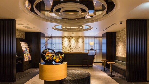 Eine moderne Lobby mit einer Rezeption, einem großen abstrakten Kunstwerk, einer runden Leuchte und einer Sitzecke.