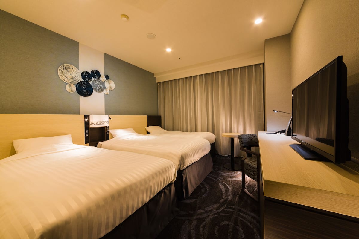 Habitación de hotel con dos camas, un escritorio con computadora, un televisor y una pared decorada con placas.