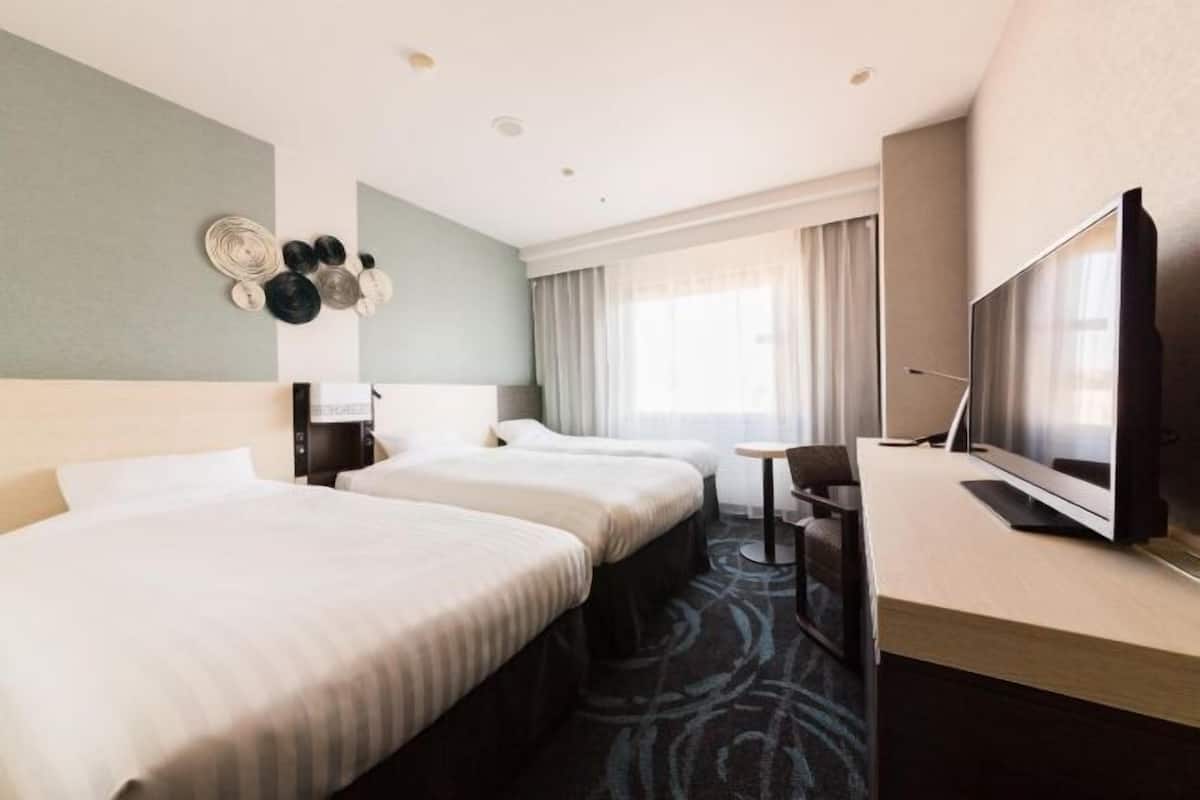Habitación de hotel con dos camas, un escritorio, televisor y ventana con cortinas.