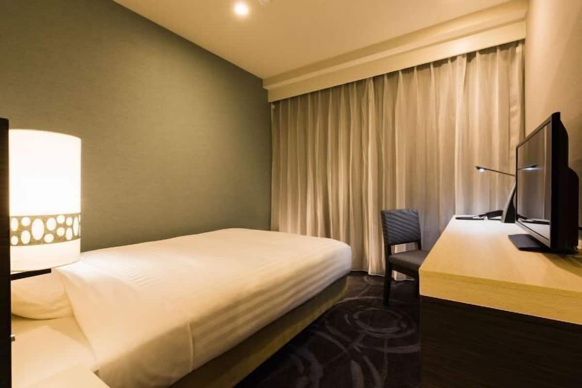 Una habitación de hotel con una cama, un escritorio con televisor, una silla y una lámpara.