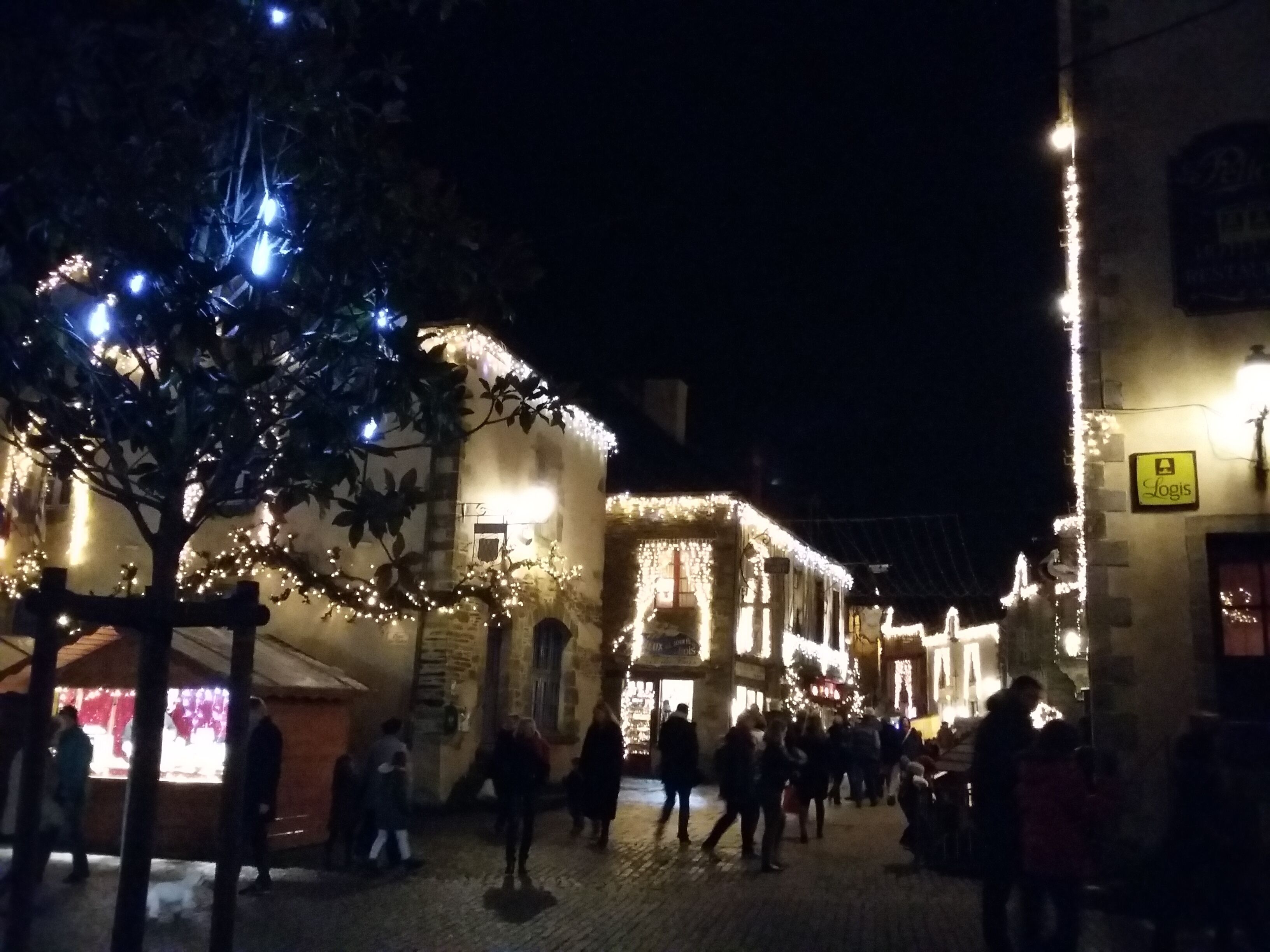A historic building with a stone facade, illuminated by string lights and a sign reading "Logis".