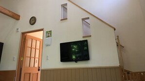 A staircase with wooden beams, a wall-mounted clock, a calendar, and a TV screen displaying a forest scene. - Guests & Dogs House Hale Ilio (Ito)