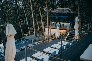 A rooftop bar with lounge chairs and umbrellas, surrounded by trees.