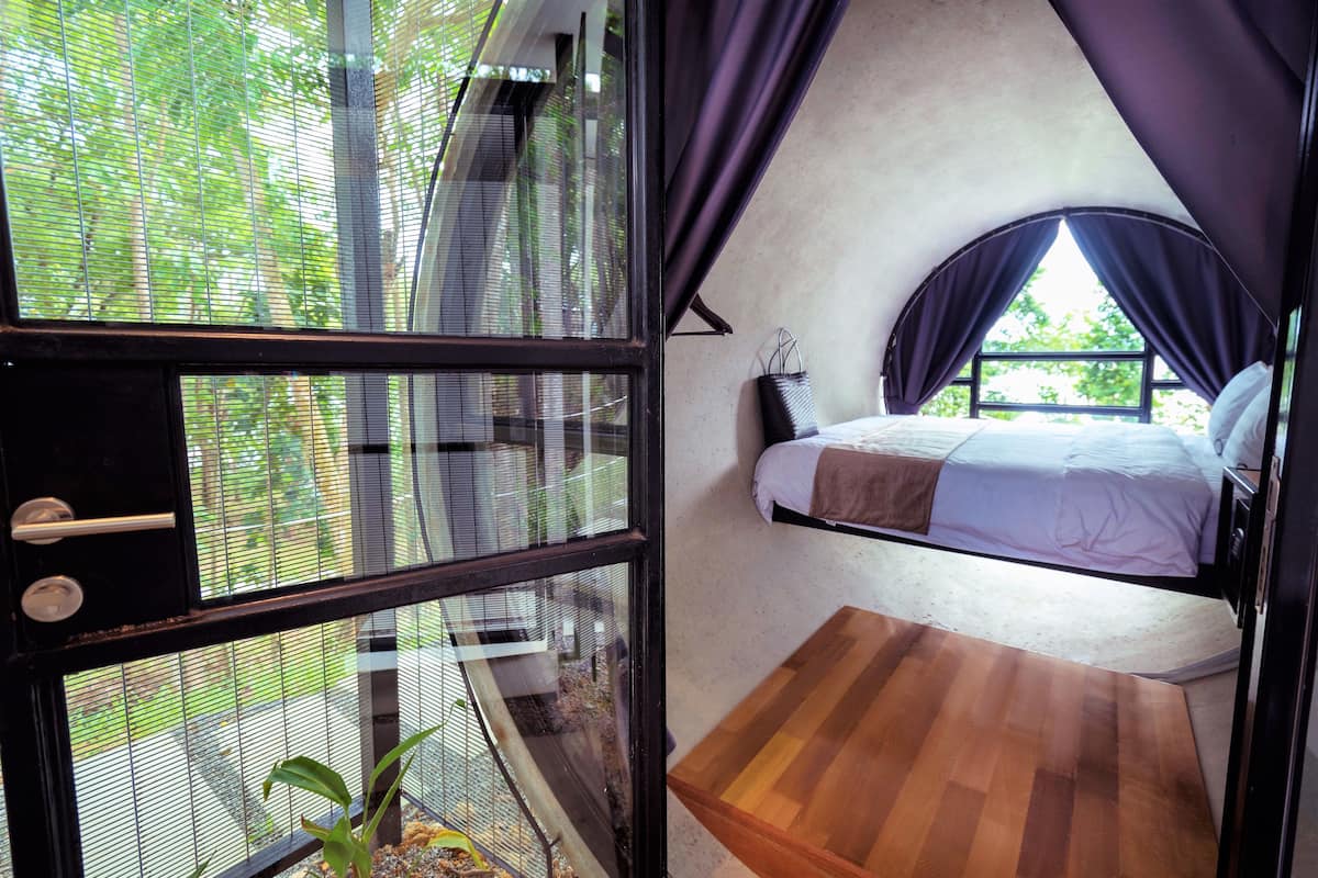 A room with a bed, a small wooden table, and a window with curtains.