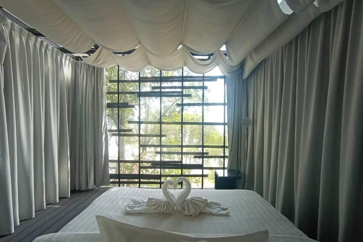 A hotel room with a bed, a heart-shaped towel arrangement, and a view through a window with a wooden lattice.
