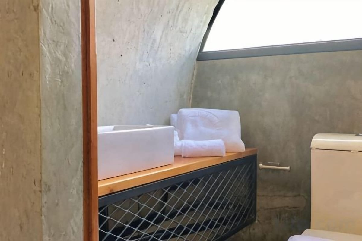 Un baño pequeño con un estante de madera que sostiene toallas, un separador de metal tipo celosía y un inodoro.