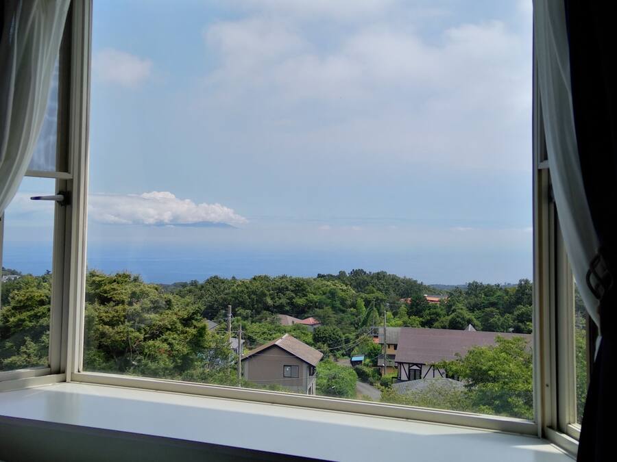 A room with a large window overlooking a residential area and a distant view of the sea.