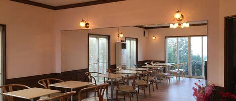 A dining area with wooden tables and chairs, large windows, and a mirror reflecting the space.