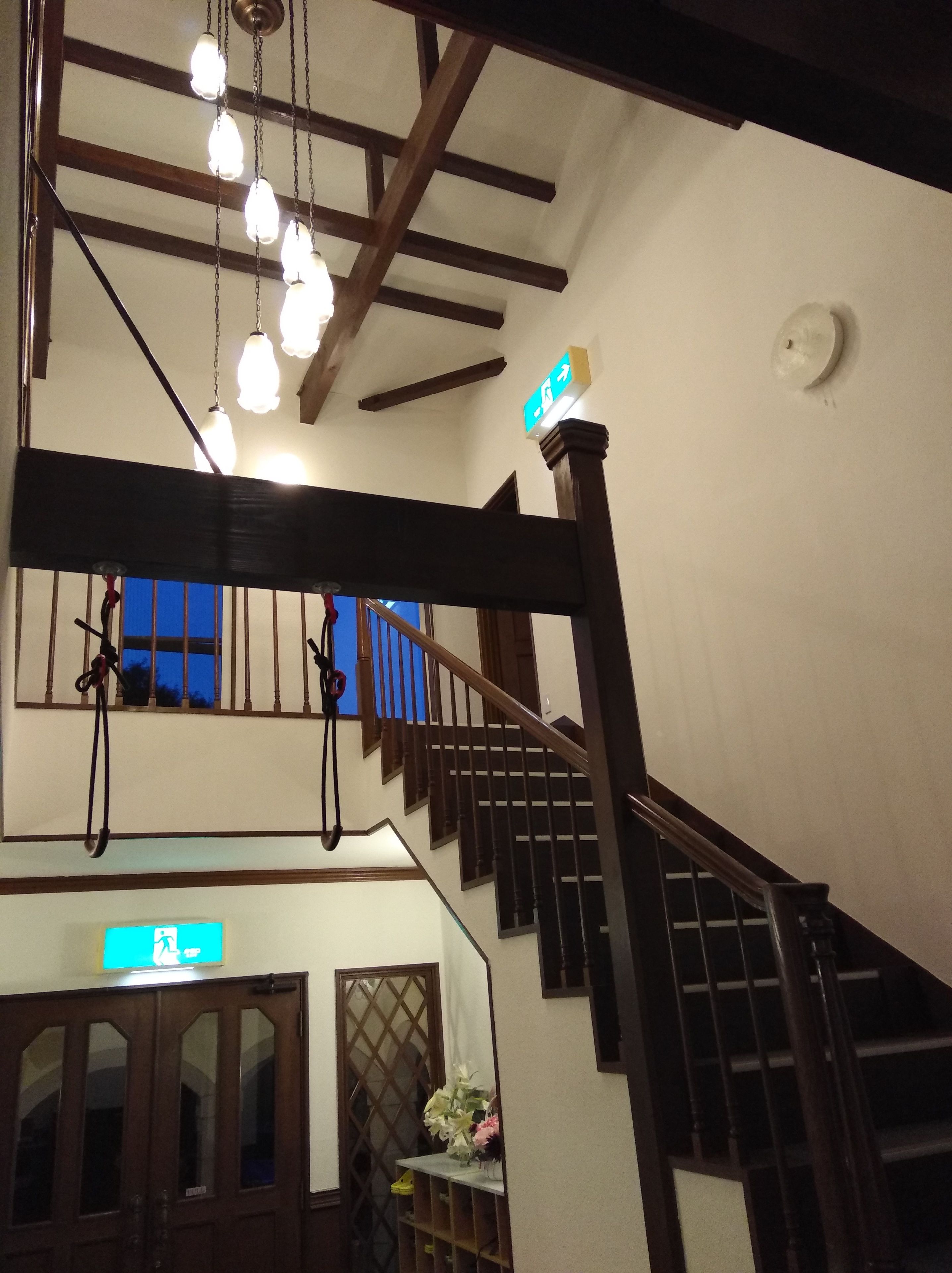 A staircase with wooden railings and a handrail, leading to a landing with a blue window and a door with a sign.