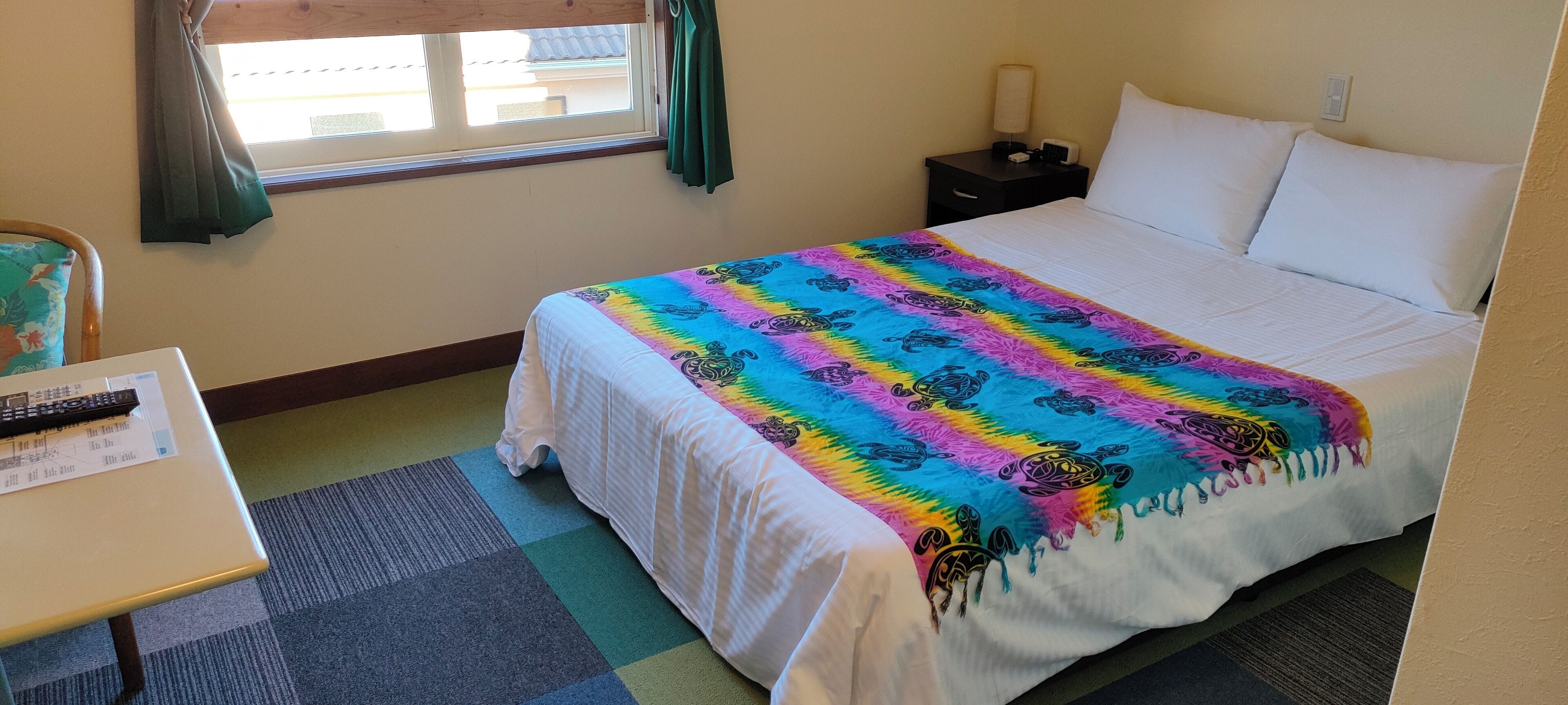 A hotel room with a large bed, a bedside table with a lamp, a chair, and a window with curtains.