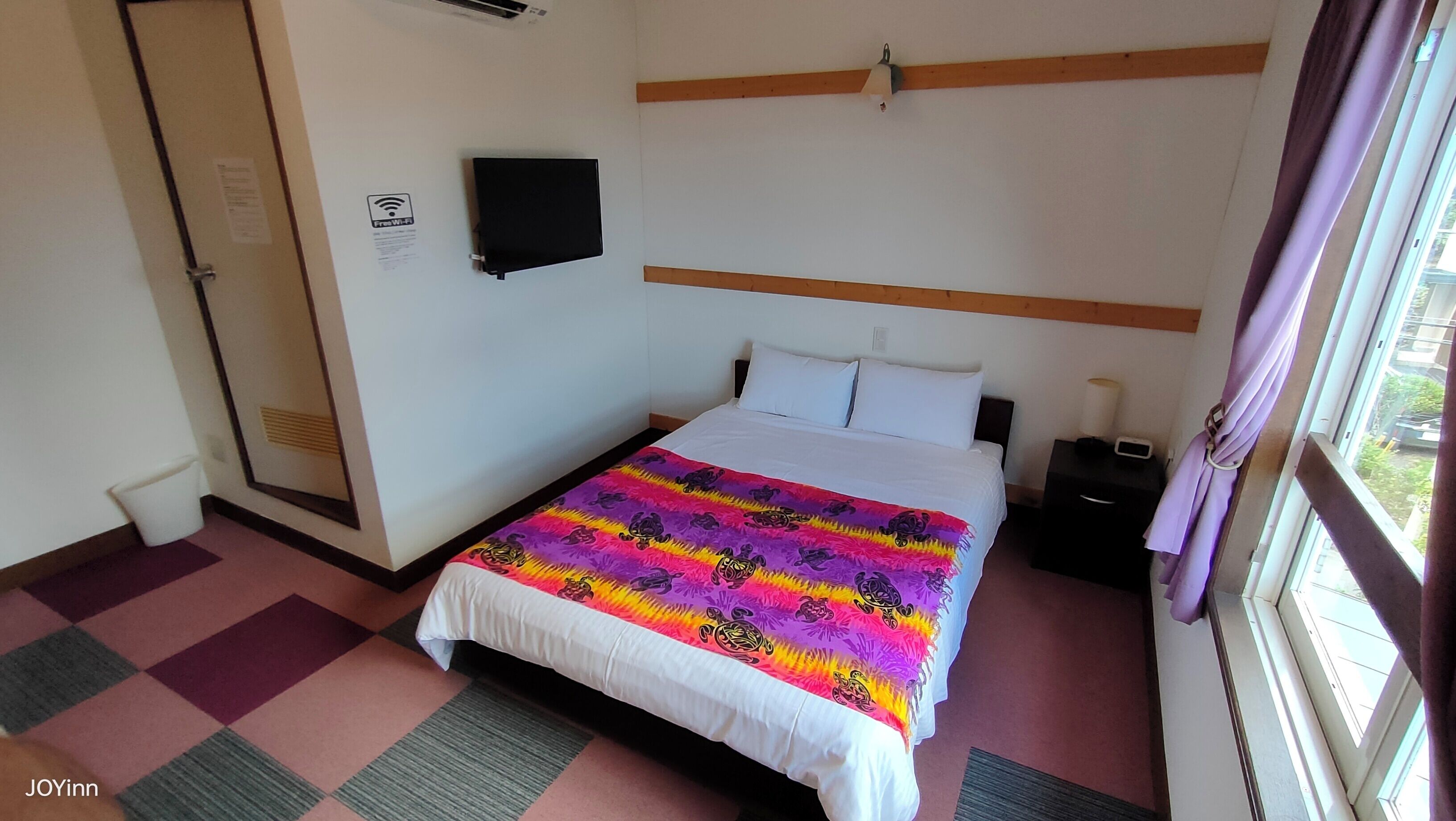 A hotel room with a bed, a TV mounted on the wall, and a window with curtains.