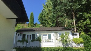 A white building with a tiled roof, surrounded by dense green foliage and tall trees.
