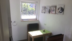 A small, bright room with a window, a table, a chair, and a radiator.