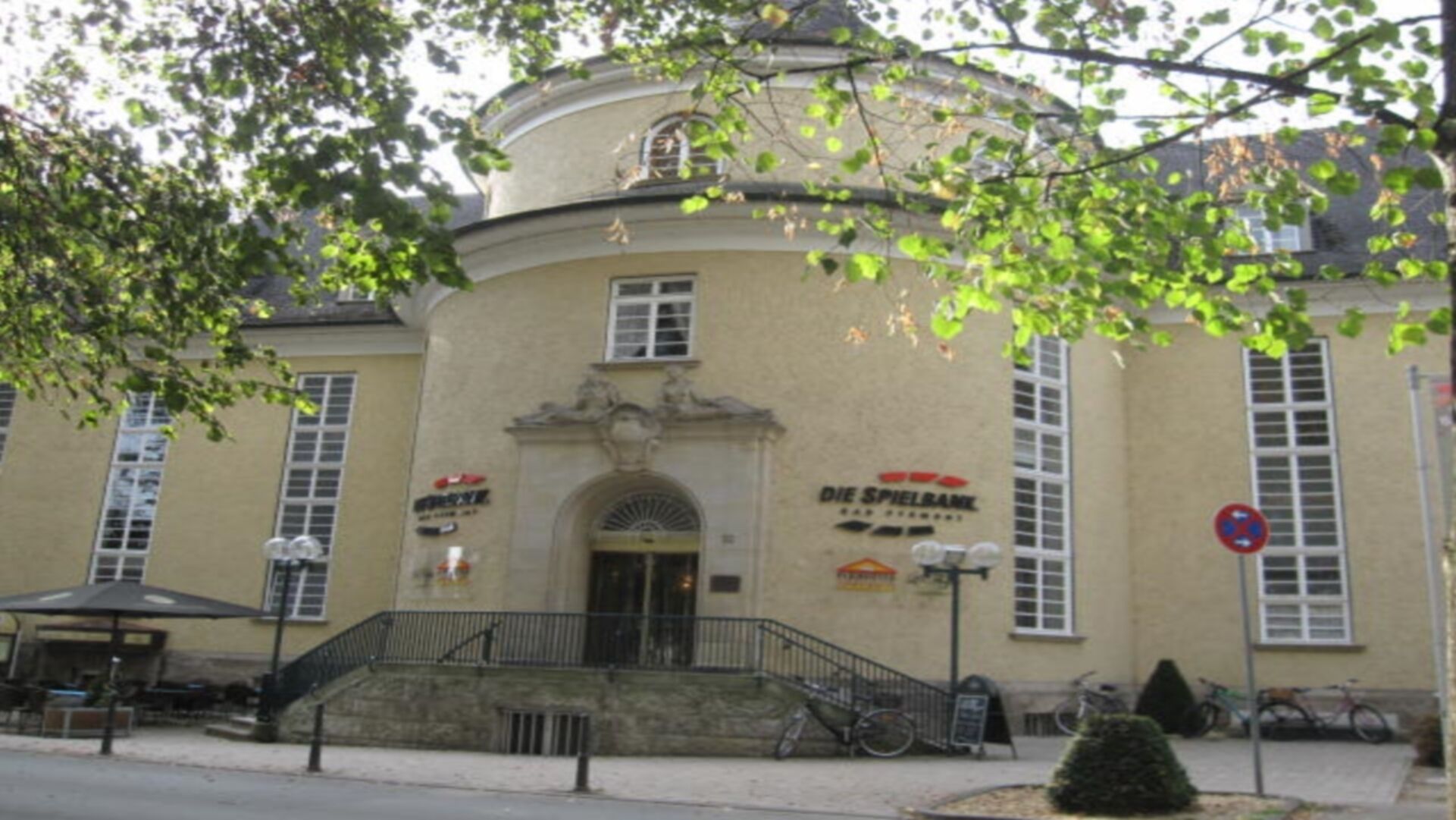 A building with a curved facade, a central entrance, and a sign for 'Die Spiehlbank'.