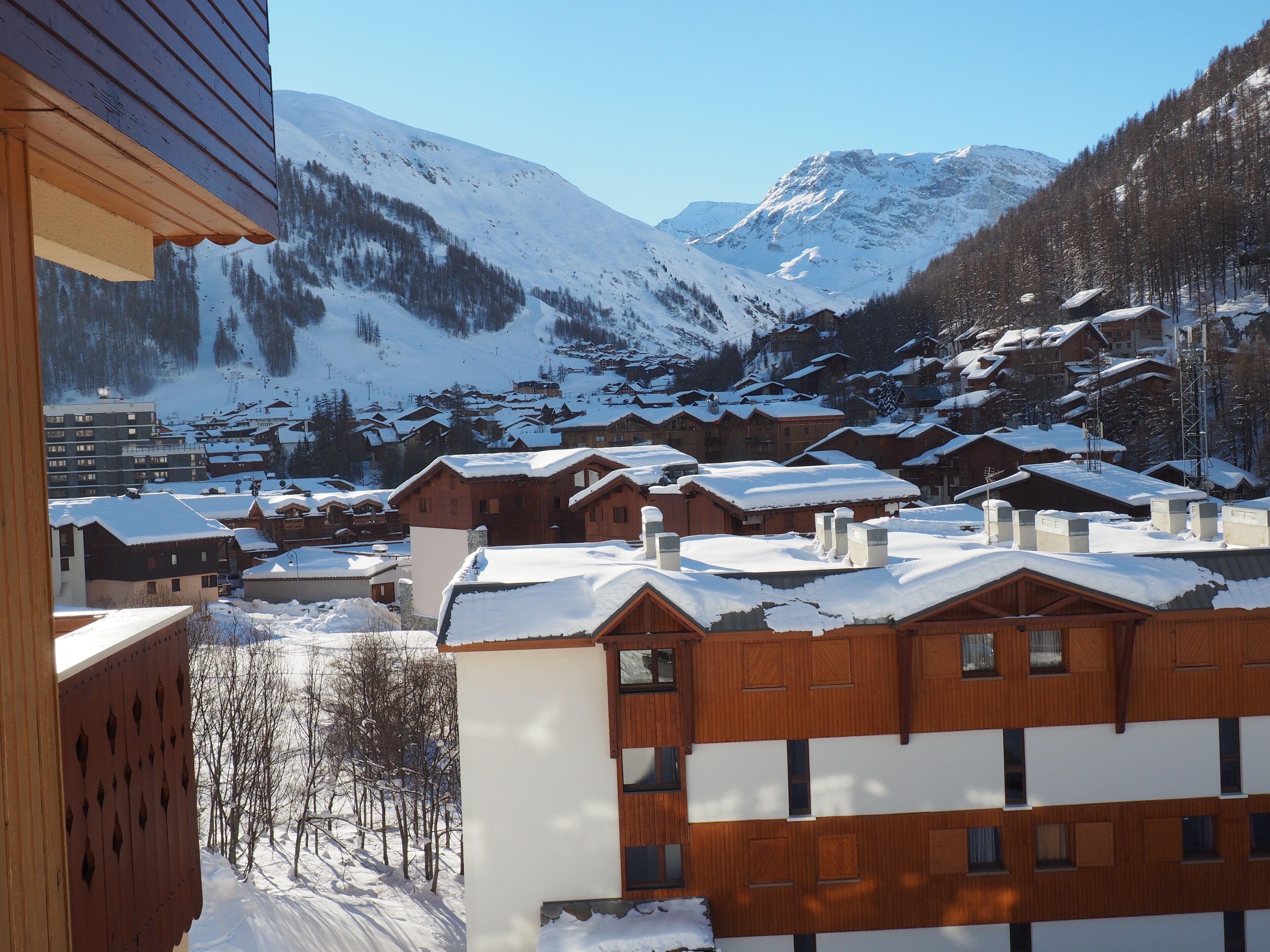 A snow-covered mountain village with wooden buildings and a clear view of the surrounding mountains.