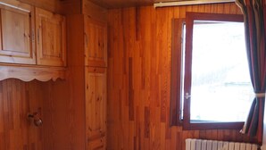 A wooden cabin room with a bed, a window, and a radiator. - 3 comfortable and bright rooms, beautiful view of Solaise and the Daille (Val-D'isère)