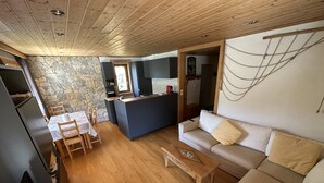 A modern living room with a stone wall, wooden flooring, a sofa, a coffee table, and a dining area with a table and chairs. - 3 comfortable and bright rooms, beautiful view of Solaise and the Daille (Val-D'isère)