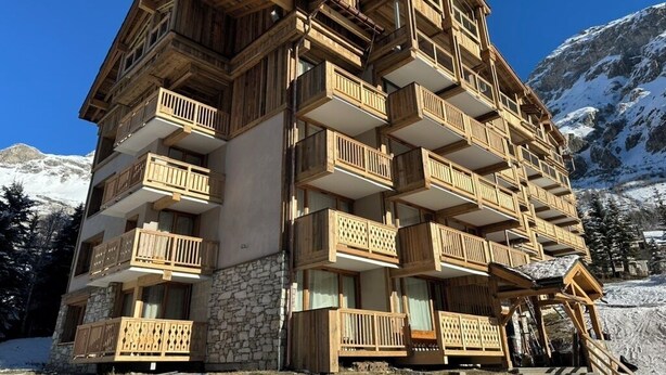 A multi-story wooden building with balconies, set against a snowy mountain backdrop. - 3 comfortable and bright rooms, beautiful view of Solaise and the Daille (Val-D'isère)