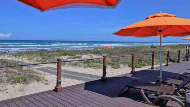 A wooden deck with orange umbrellas overlooking the beach. - 5BR/5BA Large Family Luxury Beachfront Condo, Private Terrace & Pool (South Padre Island)