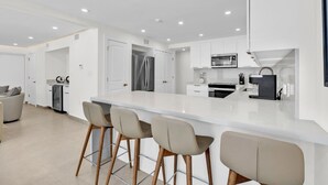 A modern kitchen with white cabinetry, a central island with bar stools, and recessed ceiling lighting. - 5BR/5BA Large Family Luxury Beachfront Condo, Private Terrace & Pool (South Padre Island)