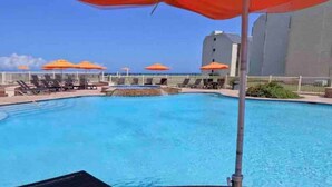 A swimming pool with lounge chairs and umbrellas, surrounded by a wooden deck and a white fence. - 5BR/5BA Large Family Luxury Beachfront Condo, Private Terrace & Pool (South Padre Island)