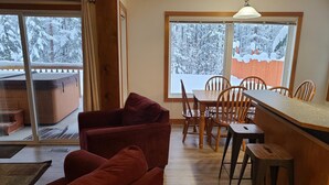 Ein gemütliches Zimmer mit Holztisch und -stühlen, einer roten Couch und einem großen Fenster mit Blick auf Schnee.