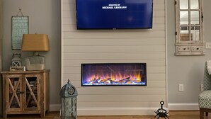 Un salon avec un téléviseur à écran plat fixé au-dessus d’une cheminée, un meuble en bois, une lampe et une lanterne décorative.