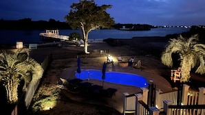 Un jardin avec une piscine, du mobilier d’extérieur et une vue sur un lac au crépuscule.