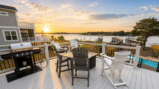 Une terrasse avec un barbecue, des chaises et une table, donnant sur une étendue d’eau.