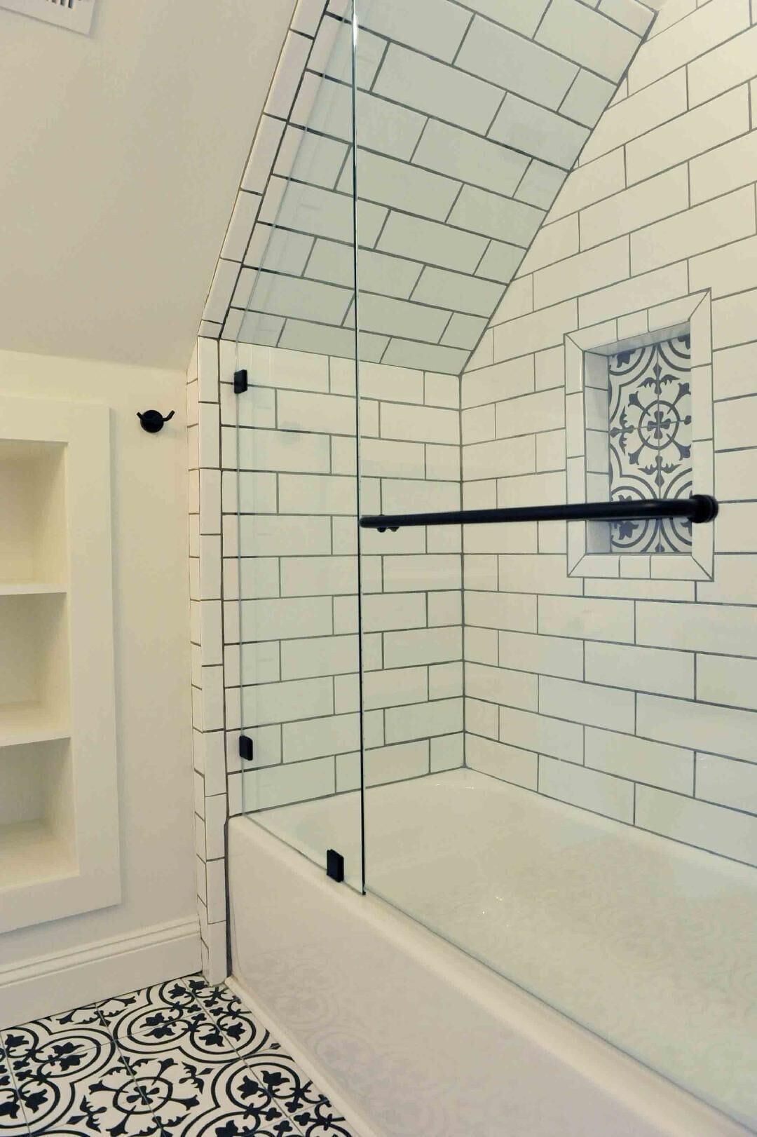 Une salle de bain avec des carreaux de céramique blancs rectangulaires, une douche en verre et un porte-serviettes noir.
