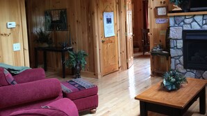 A wooden interior with a fireplace, a staircase, and a seating area with a red sofa. - Beautiful Creekside Cabin 3 Bedroom Robbinsville, NC Perfect Family Location! (Robbinsville)