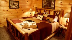 Een slaapkamer in hout met een groot bed, twee kussens, een nachtkastje en een lamp.