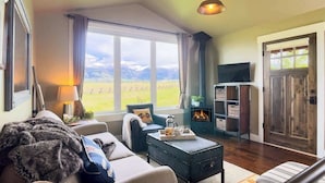 A cozy living room with a fireplace, a television, and a view of a field through large windows.