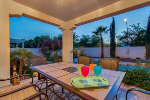 An outdoor patio with a table set for four, surrounded by chairs, and a pool in the background.