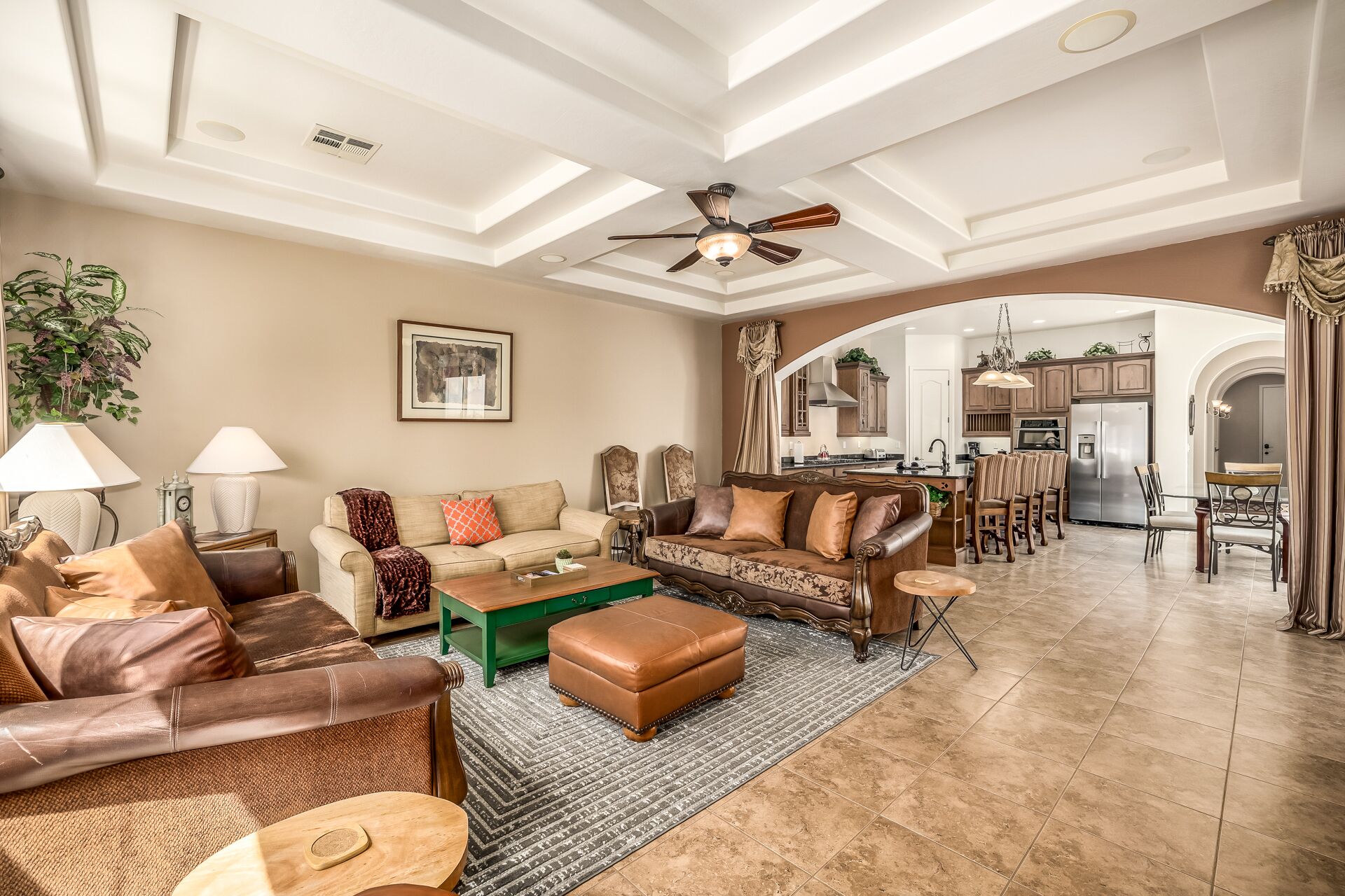 A spacious living room with a high ceiling, a ceiling fan, and a view into the kitchen through an archway.