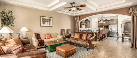 A spacious living room with a high ceiling, a ceiling fan, and a view into the kitchen through an archway.