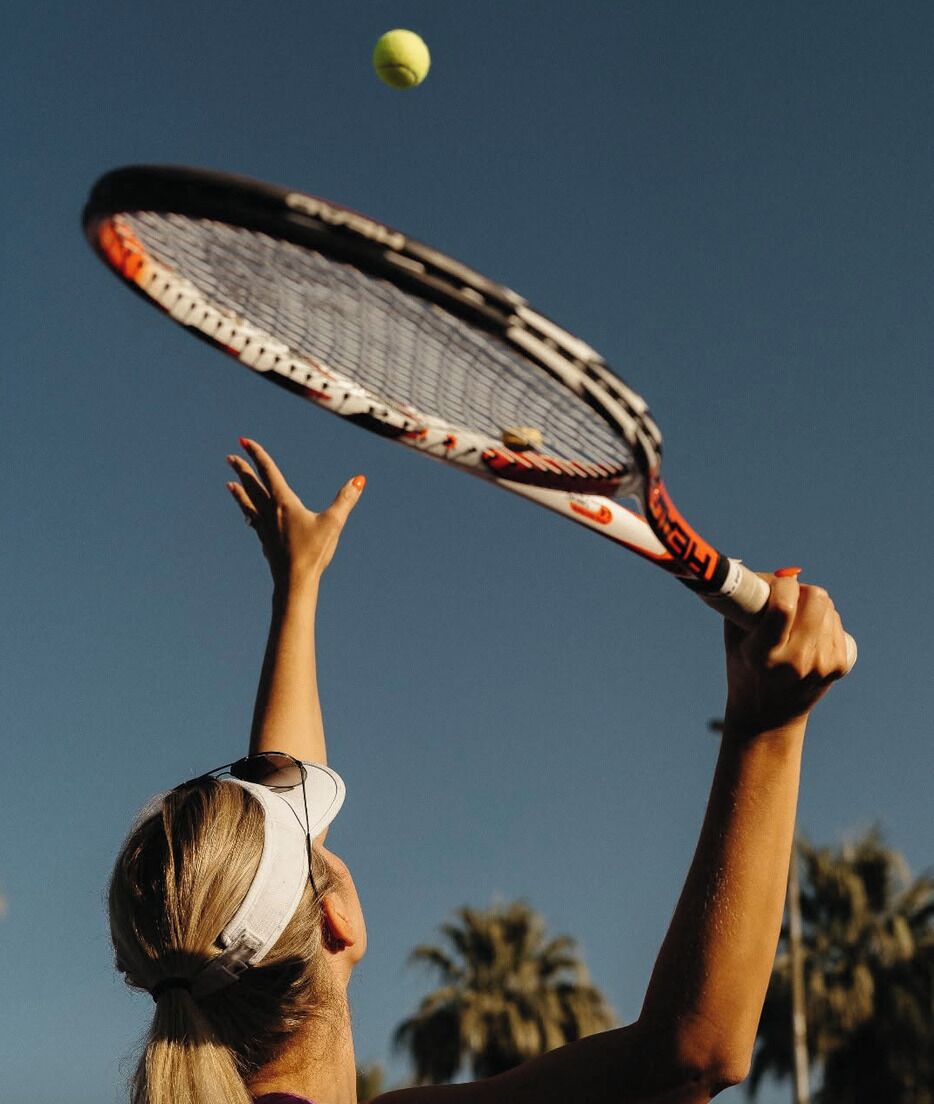 A person holding a tennis racket with a yellow tennis ball in the air.