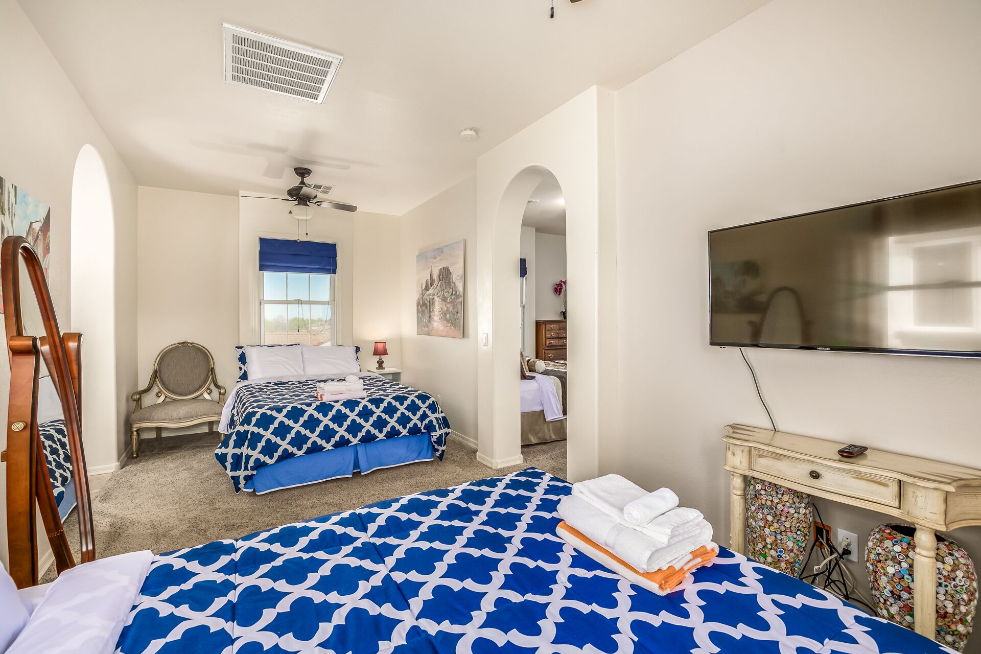 A hotel room with two beds, a ceiling fan, a TV, and a decorative wall piece.