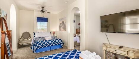 A hotel room with two beds, a ceiling fan, a TV, and a decorative wall piece.